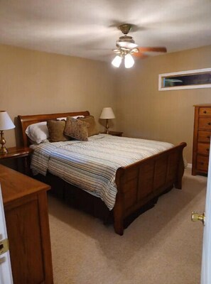 Une chambre à coucher avec un lit en bois, deux tables de chevet avec des lampes, un ventilateur de plafond et une commode.