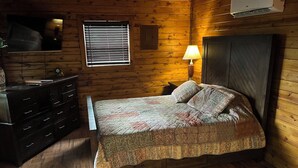 Een kamer met houten lambrisering, een bed, een dressoir en een wandtelevisie.