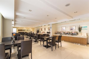 Un comedor de hotel moderno con múltiples mesas y sillas, una barra central con dispensadores de comida y un interior limpio y bien iluminado.
