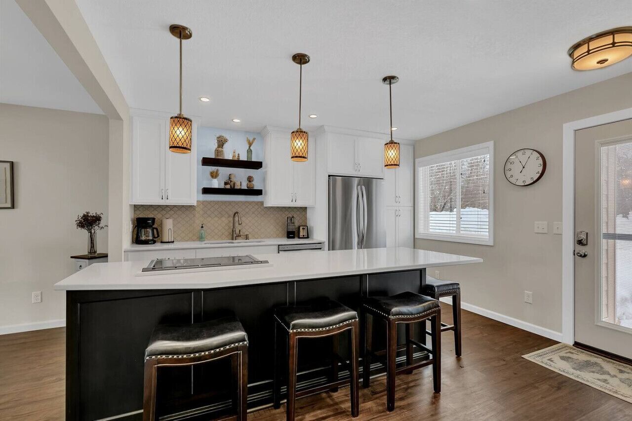 A modern kitchen with a large island, pendant lighting, and a refrigerator.
