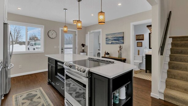 A modern kitchen with a central island, pendant lighting, and a view of the outside through a window.