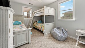 Ein Kinderzimmer mit Etagenbetten, einem Deckenventilator, einem großen Fenster und einem Korbstuhl.
