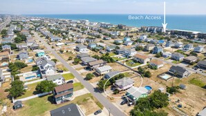 Luftaufnahme eines Wohngebiets mit Häusern, einer Straße und einem mit einem Pfeil markierten Zugang zum Strand.