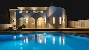 A modern house with a swimming pool, featuring a patio with lounge chairs and a well-lit interior. - Villa Beleza - Elegant Villa on Penina Golf Course (Alvor)