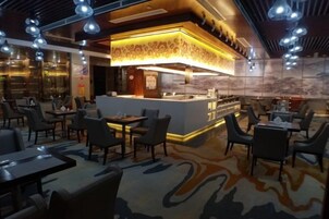 Un restaurante con zona de bar, diversas disposiciones de asientos y alfombra estampada.