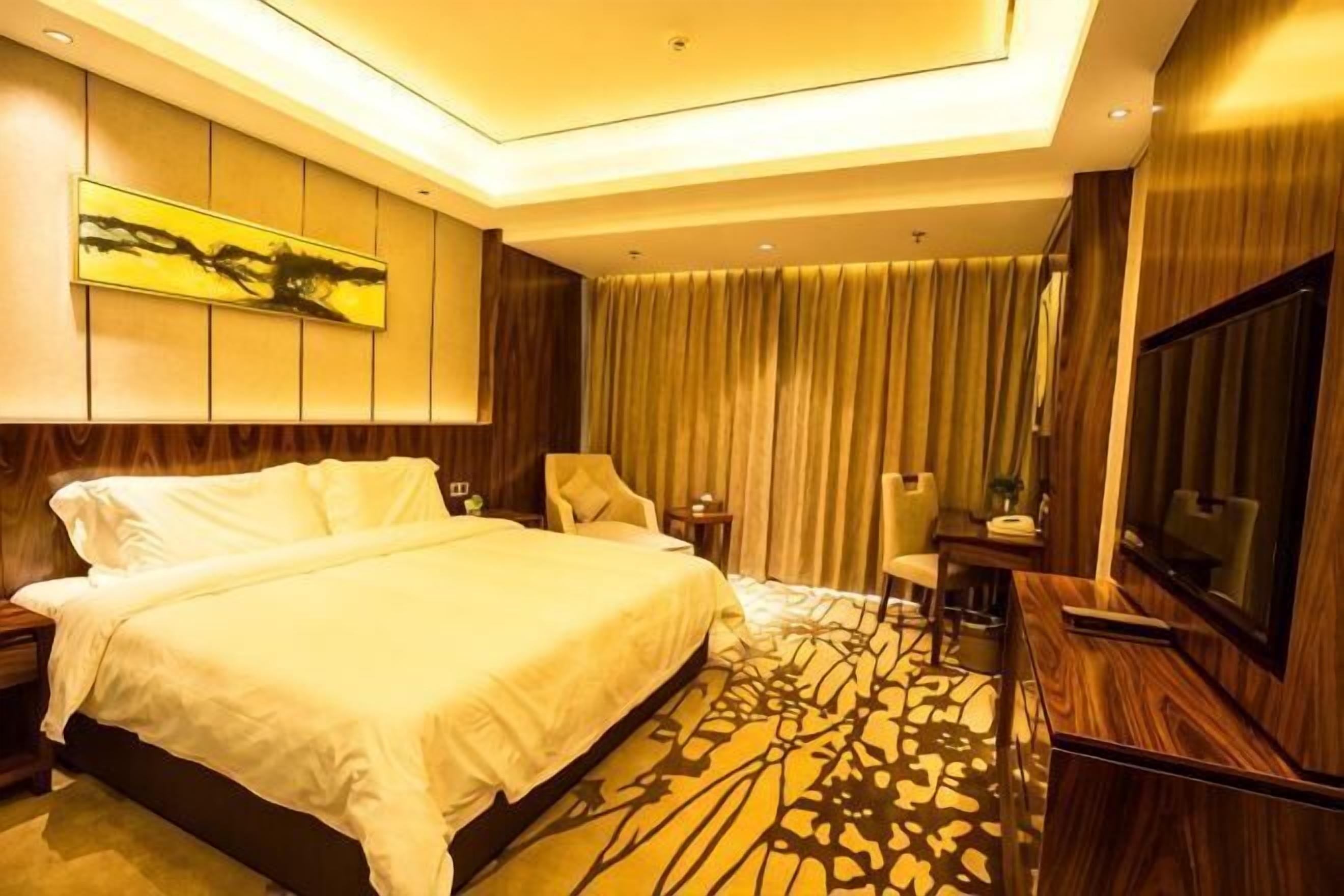 Ein Hotelzimmer mit einem großen Bett, einem Flachbildfernseher, einem Schreibtisch mit Stuhl und einem großen Fenster mit Vorhängen.