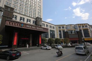 A hotel entrance with a sign, a parking lot, and a tall building in the background.