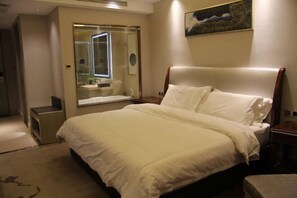 A hotel room with a large bed, a bedside table, a mirror, and a painting on the wall. - Houde Hotel (Yifeng)