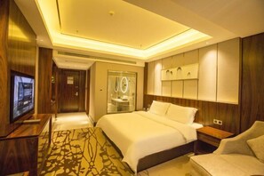 A modern hotel room with a large bed, a TV, a bathroom with a glass door, and a wooden floor. - Houde Hotel (Yifeng)