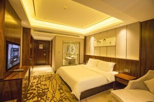 Una habitación de hotel moderna con una cama grande, televisión, baño con puerta de vidrio y piso de madera.