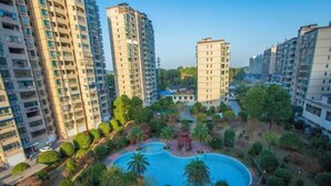 Un complejo residencial con edificios de apartamentos de gran altura, una piscina central rodeada de vegetación y un pequeño pabellón.