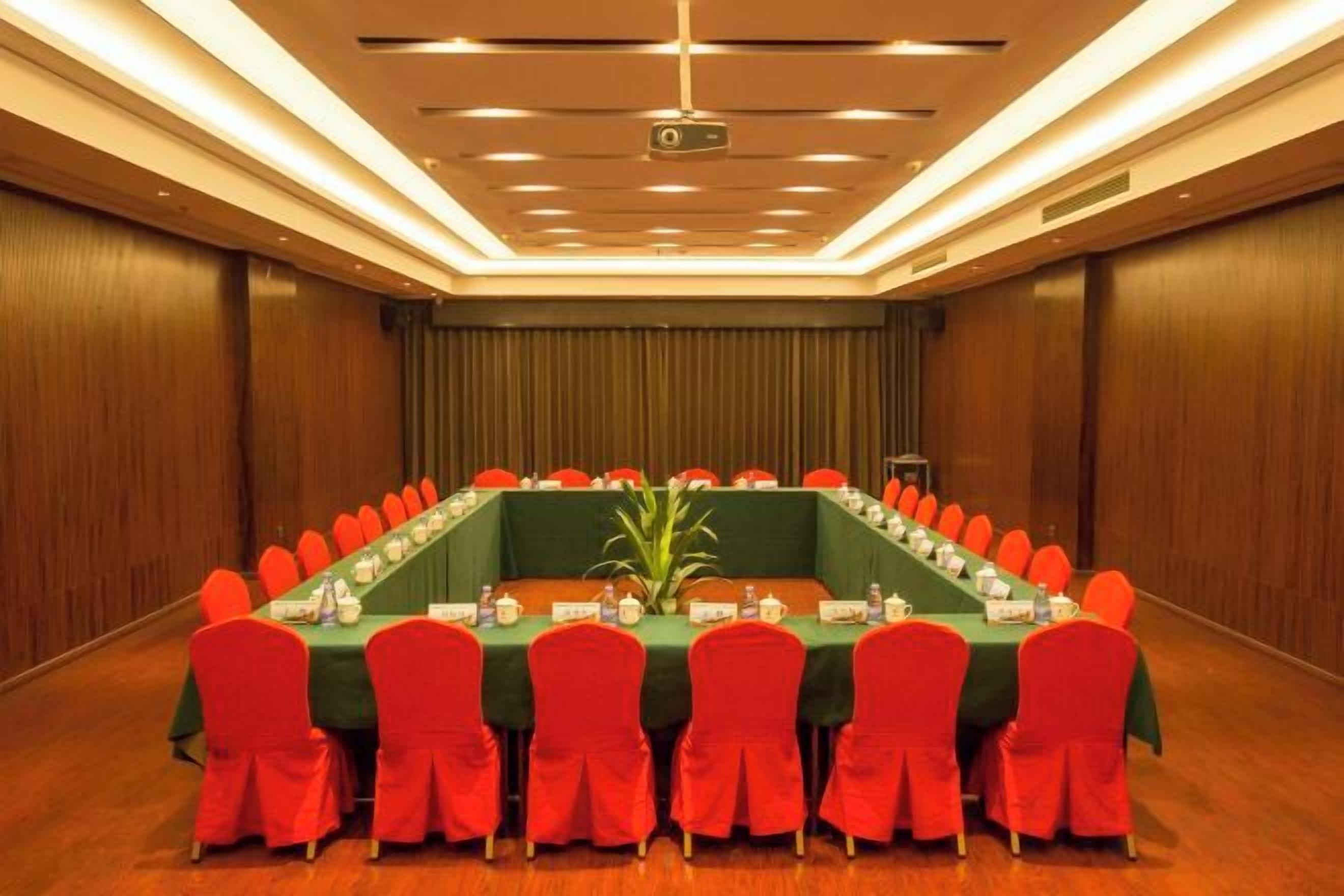 A conference room with a long table, red chairs, and a projector screen.