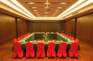 Un salón de conferencias con una larga mesa, sillas rojas y una pantalla para proyector.