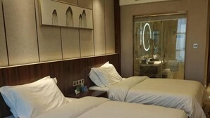 Habitación de hotel con dos camas, un espejo, tocador y vistas al exterior.