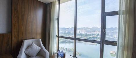 A room with a large window, a chair, a small table with bottles, and a view of a cityscape and river.