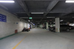 A parking garage with concrete pillars, directional signs, and parked vehicles. - Houde Hotel (Yifeng)