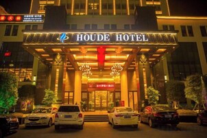El exterior del Hotel Houde, con una entrada destacada, un cartel rojo y varios autos estacionados frente al hotel.