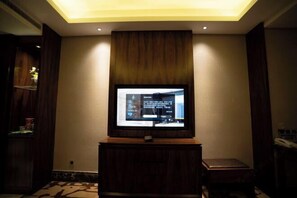 A television mounted on a wooden stand in a room with a ceiling light and a small table beside it. - Houde Hotel (Yifeng)
