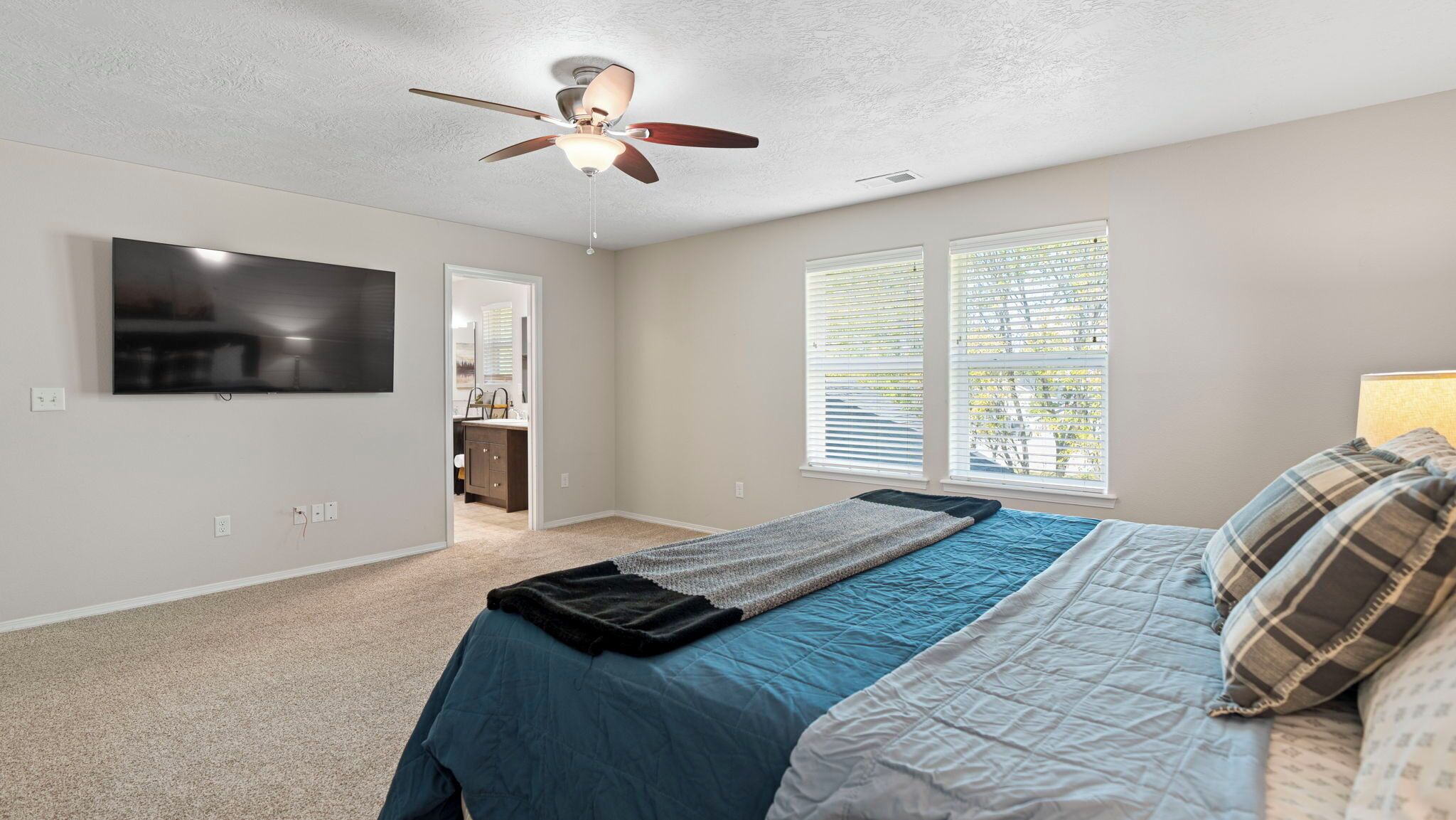 A bedroom with a bed, a ceiling fan, a TV, and a window with blinds.