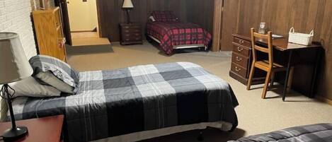 Un dormitorio con dos camas, un aparador, un escritorio y una puerta que da a otra habitación.