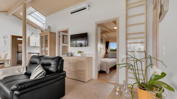 A modern living room with a black leather sofa, wooden flooring, and a dining area with a wooden table and chairs. - Amazing home in Sydals with WiFi (Sydals)