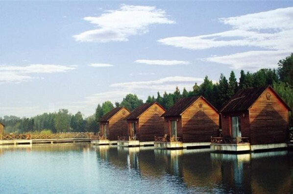 Cabins sit elevated over a serene lake, offering access via a wooden dock.
