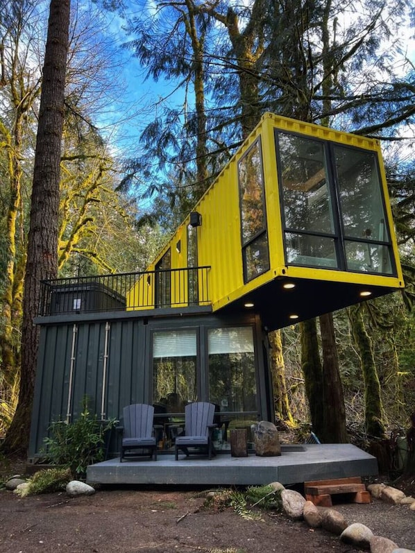 A modern cabin with a yellow upper level, a deck with chairs, and a forest backdrop. - Sea Containers-Hot Tub/Steam/Sauna/Cold Plunge (Index)