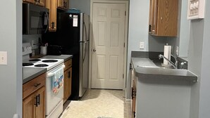 Una cocina compacta con armarios de madera, un refrigerador negro, un microondas y una estufa.