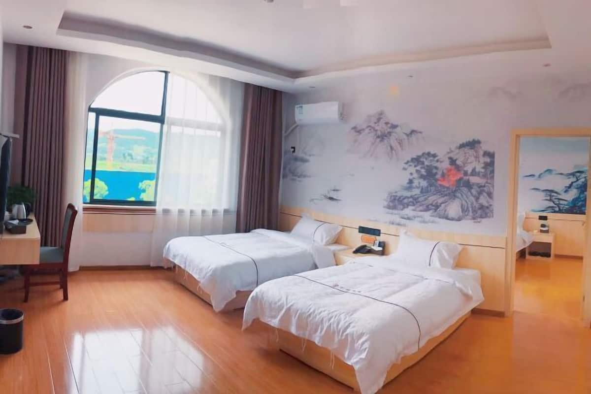 A hotel room with two beds, a desk, a chair, a window with curtains, and a wall with a painting.
