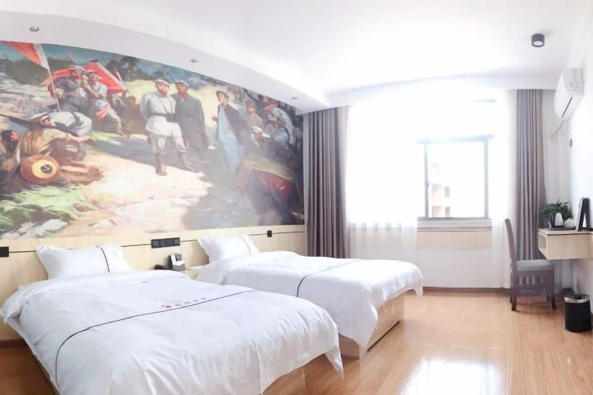 A hotel room with two beds, a large mural on the wall, a desk with a chair, and a window providing natural light.