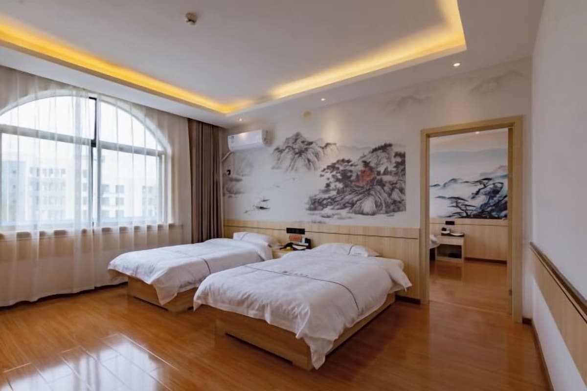 Quarto de hotel com duas camas, uma janela grande com cortinas, um mural na parede e um espelho.
