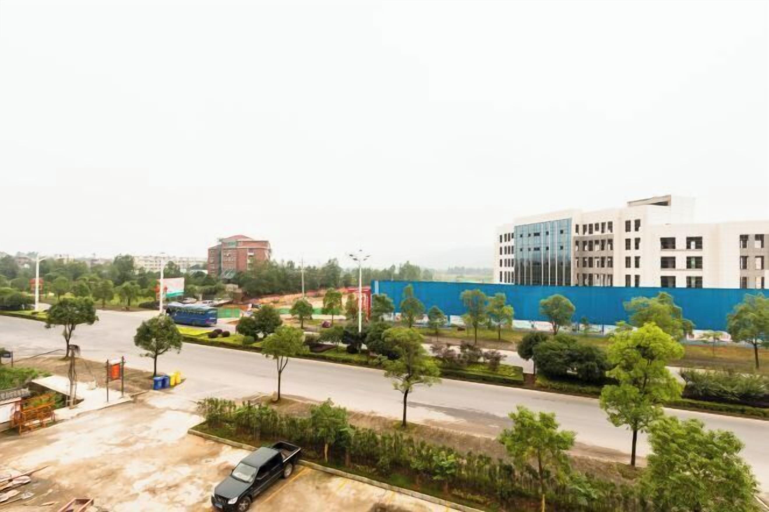 A modern building with a blue facade, surrounded by trees and a parking lot.