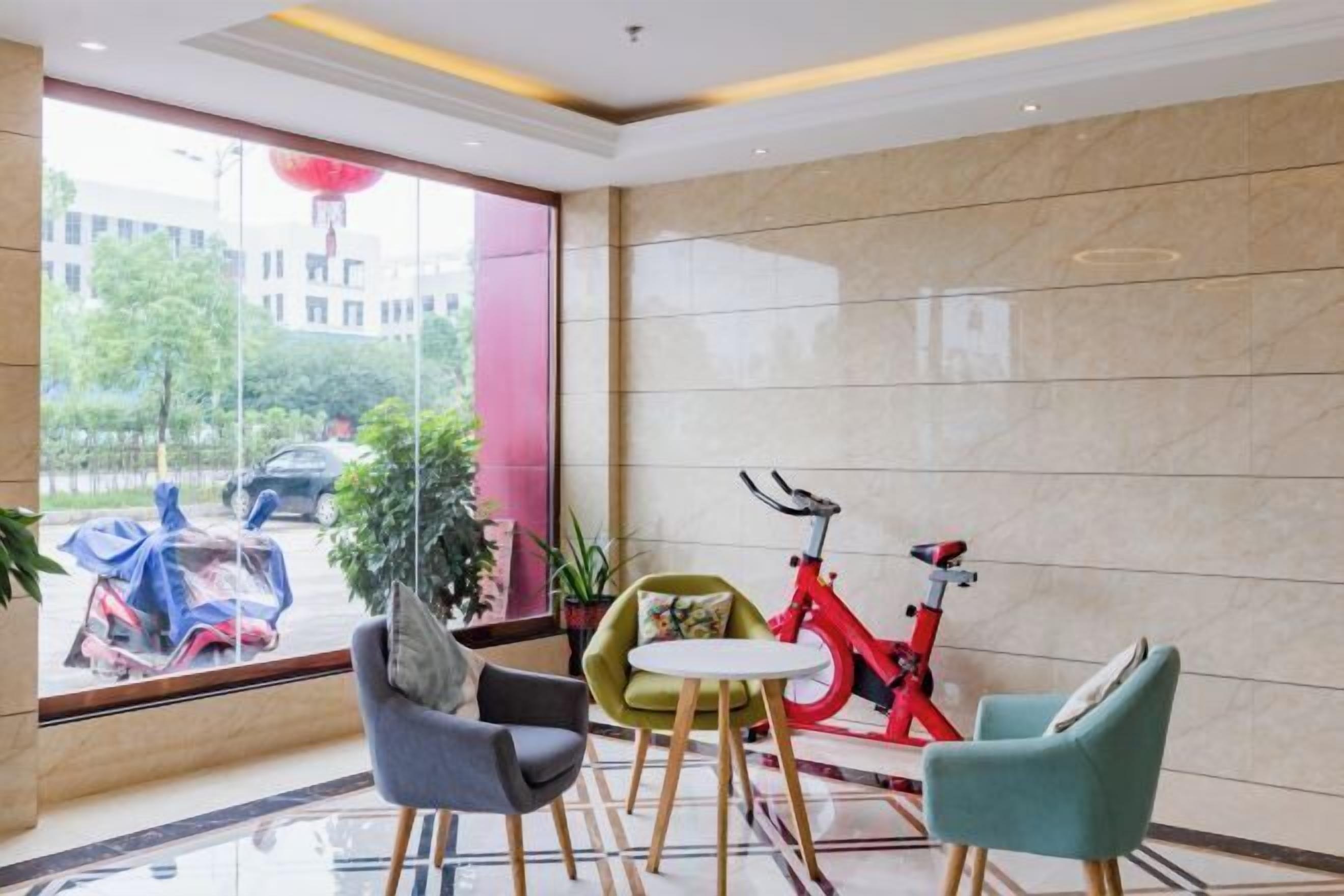 A modern hotel lobby with a large window, a red stationary bike, and three chairs.