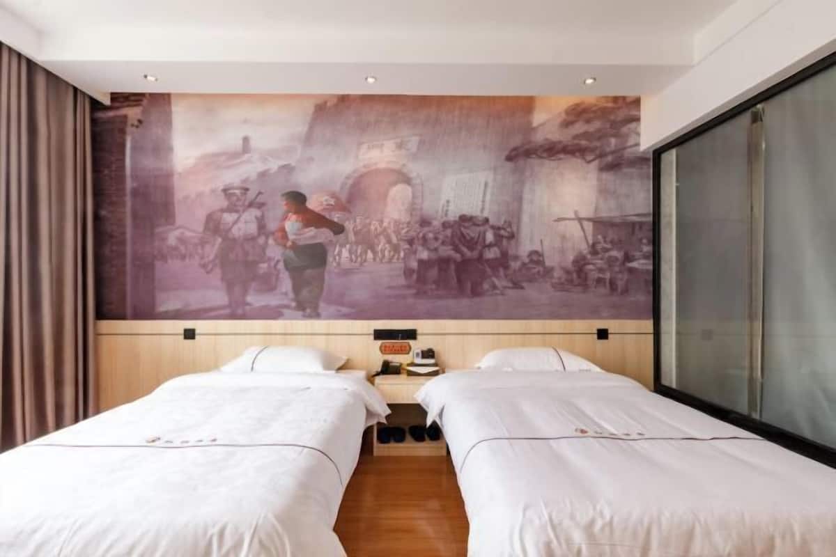 A hotel room with two beds, a mural on the wall, and a large window.