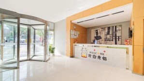 A hotel reception area with a glass revolving door, a reception desk with a 'WELCOME' sign, and a view of the outside through the glass doors. - Jinjiang Inn (Shanghai International Tourist Resort Kangxin Highway) (Shanghai)