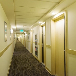 Ein Hotelgang mit Teppichböden, Türen auf beiden Seiten und einem Schild, das den Weg zum Aufzug weist.