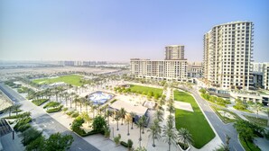 A modern urban area with high-rise buildings, a central plaza with palm trees, and a large open space with a blue structure. - Sophisticated 1BR at Town Square Rawda by Deluxe Holiday Homes (Dubai)