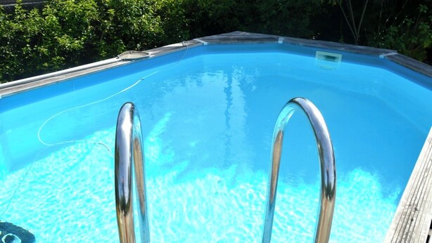 Une piscine à l’eau d’un bleu cristallin, entourée d’une terrasse en bois et dotée d’un escalier en métal.