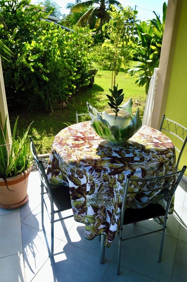 A patio with a table covered in a floral tablecloth, surrounded by metal chairs, and a potted plant.