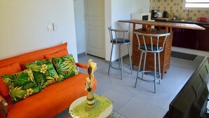 Un espace de vie compact comprenant un canapé, deux fauteuils, une petite table et un coin cuisine avec un comptoir et un évier.