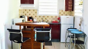 Une cuisine compacte dotée d’un îlot central, de deux tabourets de bar, d’un réfrigérateur et d’un évier.