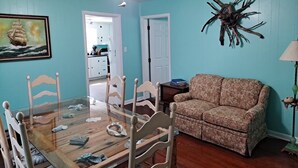 A room with a dining table, chairs, a sofa, a ceiling fan, and a wall decoration. - Seaside Retreat (Wachapreague)