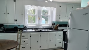 A kitchen with white cabinets, a window with a view, a refrigerator, and a dining table with chairs. - Seaside Retreat (Wachapreague)
