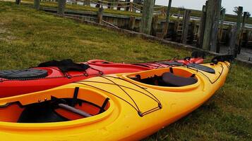 Two kayaks, one red and one yellow, parked on grass near a wooden dock.