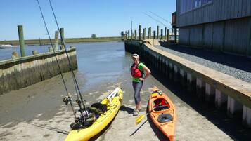 A person standing next to a yellow kayak and an orange kayak on a concrete dock by a body of water.