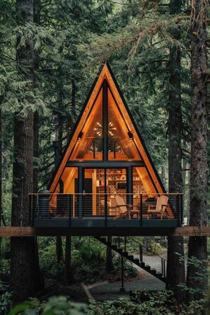 A cabin with a triangular roof, wooden deck, and a staircase leading to the entrance.