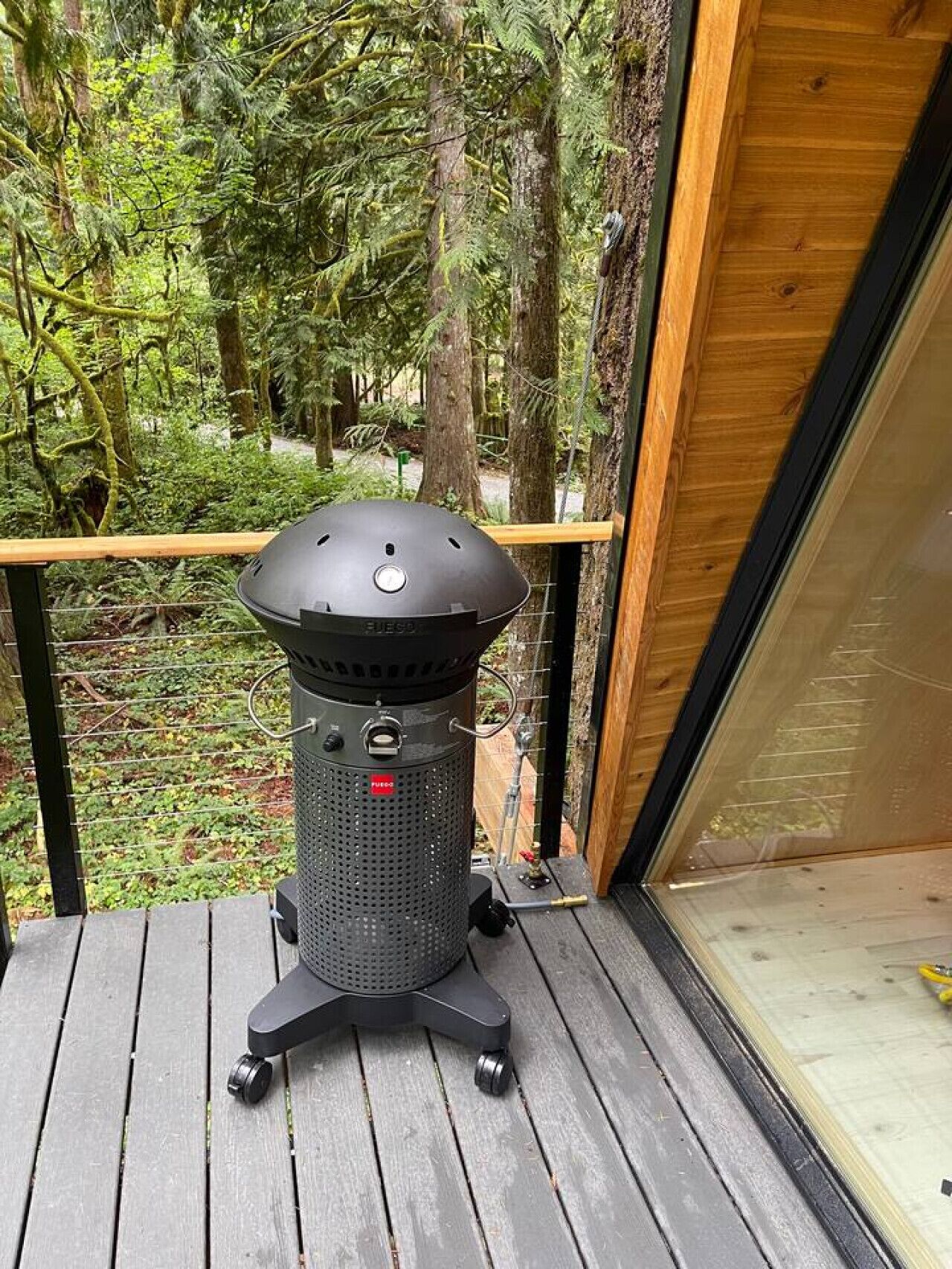 A portable grill on a wooden deck with a view of a forest.