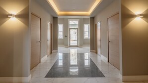 Un pasillo con suelo de mármol pulido, puertas de madera e iluminación empotrada.