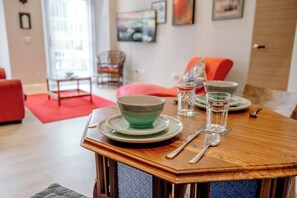 Ein Esstisch mit Tellern, Schüsseln und Besteck. Im Hintergrund stehen ein Stuhl und eine Couch.