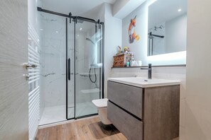 Ein modernes Badezimmer mit Duschkabine aus Glas, einer weißen Toilette und einem Waschtisch mit Spiegel.